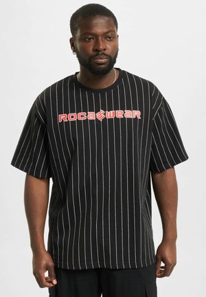 Camiseta de manga corta a rayas negras con un corte holgado, que presenta un prominente logo rojo de "ROCAWEAR" en el pecho.