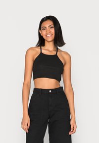 Top cropped preto com padrão canelado e alças finas, combinado com calças pretas de alta cintura, com bolsos frontais e fecho de botão.
