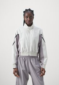Lightweight, color-blocked jacket featuring a high collar, elastic waist, and side black accents. Made of smooth, performance fabric.