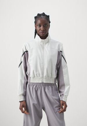 Veste légère et colorée avec un col haut, une taille élastique et des accents noirs sur les côtés. Fabriquée en tissu lisse et performant.