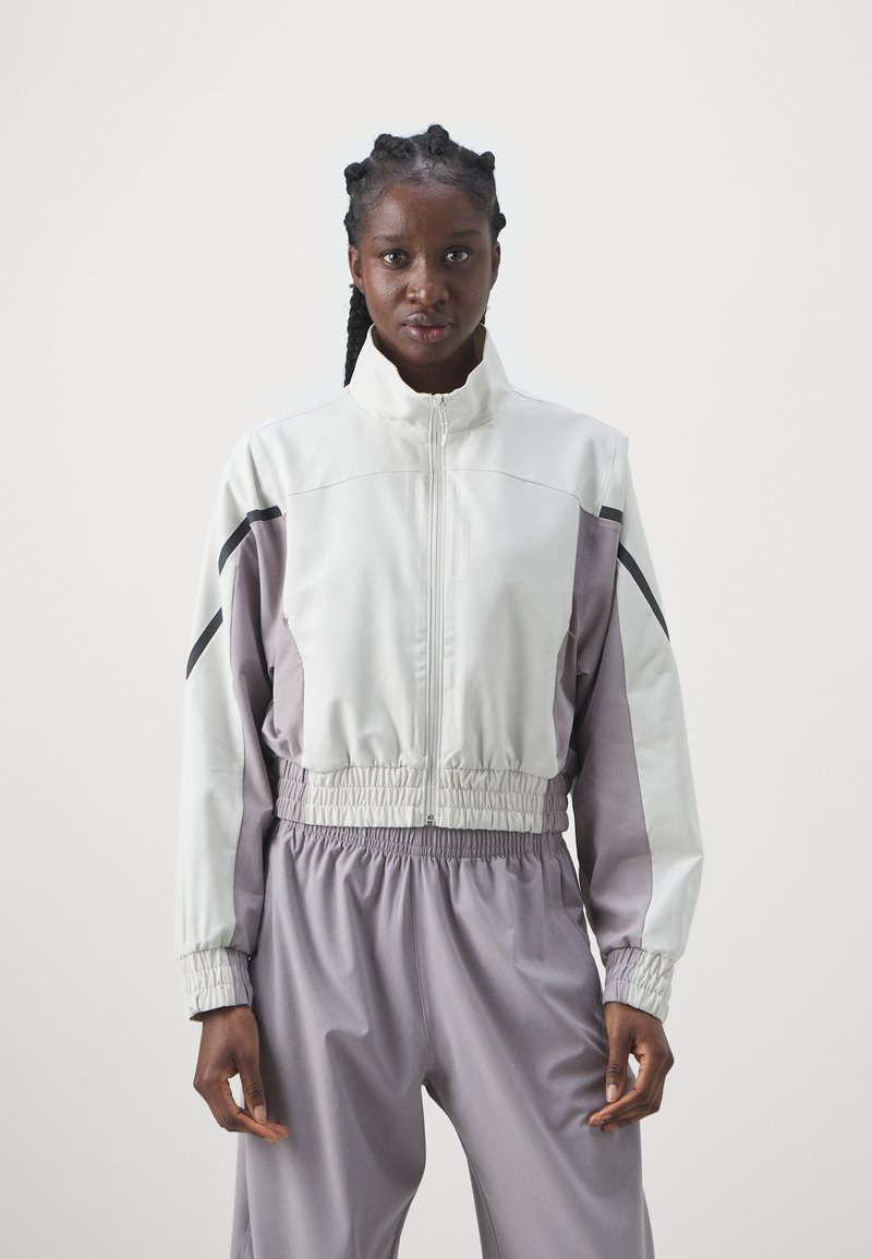 Lightweight, color-blocked jacket featuring a high collar, elastic waist, and side black accents. Made of smooth, performance fabric.