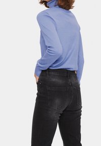 Hellblaues Rollkragenpullover mit langen Ärmeln, kombiniert mit schwarzen Jeans aus Denim, die über Rückentaschen verfügen und eine leicht verblasste Textur aufweisen.