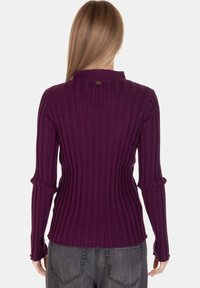 Top a coste viola con maniche lunghe, dotato di un colletto alto e un piccolo logo sul retro. Silhouette aderente.