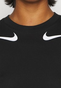 Nacken och övre bröstet av en person som bär en svart skjorta med två vita Nike-swoosh-logotyper nära kragen.