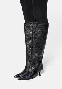 Black knee-high boots made of textured faux crocodile leather, featuring a pointed toe and a small stiletto heel.