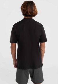 Camiseta negra de manga corta con cuello redondo, hecha de una tela suave; combinada con pantalones cortos grises, mostrando un diseño liso en la parte posterior.