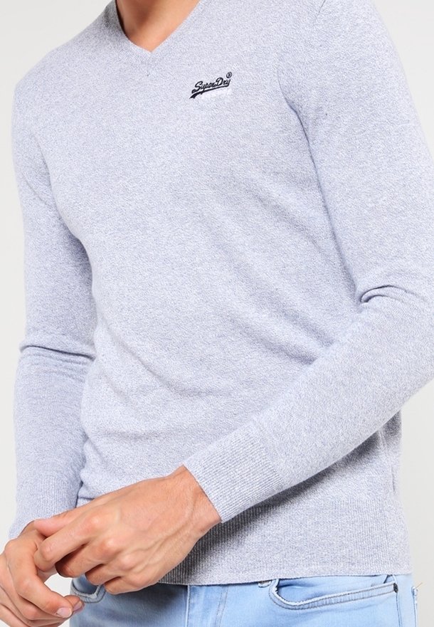 Szary sweter z mieszanki bawełny i wiskozy z długimi rękawami i dekoltem w serek, z małym czarnym logo na piersi. Tkanina dzianinowa o fakturze.