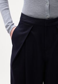 Calças de cintura alta navy com pregas e bolsos laterais, combinadas com um suéter de manga longa canelado cinza claro. Textura suave e design estruturado.