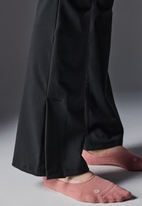 Pantaloni negri cu un croi lejer, având slituri laterale la margine. Sosete roz pal cu decolteu mic, având un model texturat.