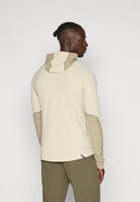Sweatshirt com capuz em bege claro, com tecido texturizado, detalhes esculpidos contrastantes e design ajustado. Mangas longas e bainha arredondada.