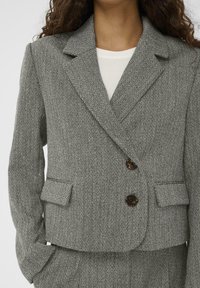 Sivi blazer z ribjim vzorcem s klasičnimi ovratniki, dvema gumboma in všitimi žepi. Tkanina ima teksturiran videz in mehak zaključek.