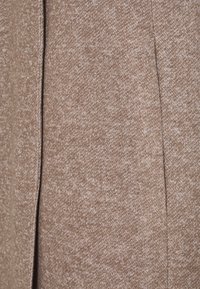Tessuto texturizzato in toni caldi di marrone, caratterizzato da un motivo sottile e un design snello con una cucitura visibile per un dettaglio strutturale.
