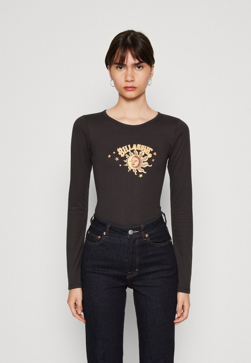 Μακρυμάνικο σκούρο γκρίζο κορμάκι με στρογγυλή λαιμόκοψη, διαθέτοντας κεντρικό γραφικό ήλιου σε ανοιχτά χρώματα και μικρά αστέρια. Συνδυάζεται με ψηλόμεσα σκούρα τζιν.