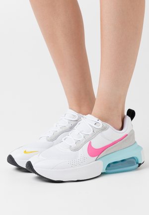 White sneakers with pink and yellow accents, leather and suede materials, cushioned sole, and visible air unit. Rounded toe and black outsole.