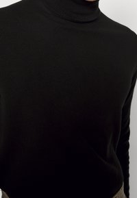 Pull à col roulé noir en tissu tricoté lisse, présentant une coupe ajustée et un col côtelé pour un détail structuré.