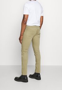 Gröna slim-fit byxor i bomullsblandning, med en medelhög midja, två bakfickor och en slät yta, i kombination med svarta ankelboots.