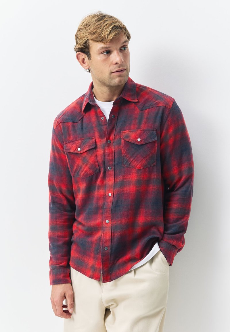 Cămașă flanelată în carouri roșu și bleumarin, cu guler cu nasturi, două buzunare la piept și închidere frontală cu nasturi; țesătura pare moale și texturată.