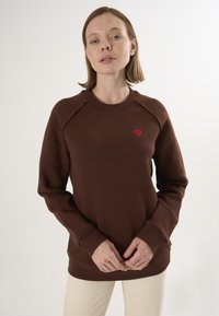 Bruine sweatshirt met geribde halslijn en manchetten, voorzien van een klein rood hartje geborduurd op de borst, met een gladde textuur.