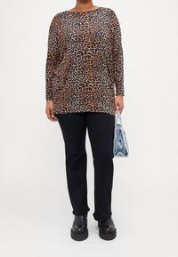 Leopardmönstrad långärmad topp i nyanser av brunt och svart, kombinerad med svarta byxor och svarta platåskor, bärande en ljusblå väska.