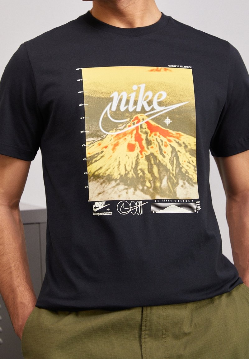 Svart bomullströja med en gul och röd berggrafik samt "Nike"-logotyp, tillsammans med mått och designdetaljer.