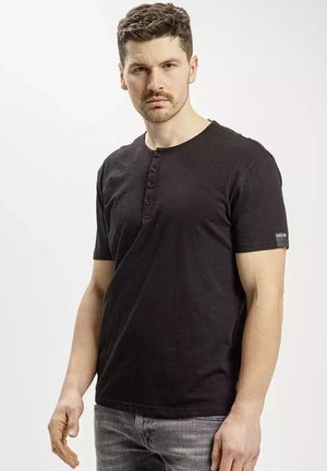 Czarna krótko rękawowa koszulka henley z pięcioma guzikami przy dekolcie. Tkanina wydaje się miękka, z delikatną teksturą. Prosty design z logiem na rękawie.