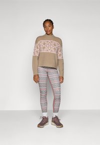 Pulover bej tricotat cu un model geometric roz, asortat cu colanți cu model în nuanțe de roz, alb și albastru. Pantofi sport maro completează ținuta.