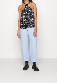 Top halter floreale nero e avorio con scollatura annodata; abbinato a pantaloni dritti blu chiaro e stivaletti neri con tacco chunky.