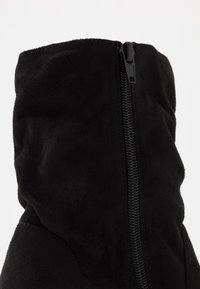 Černé semišové kotníkové boty s texturovaným povrchem, zapínáním na zip a měkkým, uvolněným střihem. Švy přispívají k celkovému designu.