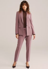 Svilena obleka sivke z modnim blazerjem po meri in ožjimi hlačami, teksturirana rjava majica spodaj in črni koničasti čevlji. Gladek material, klasična zasnova.