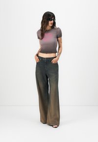 Cropped, gray-purple t-shirt with a pink heart graphic, paired with wide-leg, faded black jeans. Model wears black sunglasses and sandals.