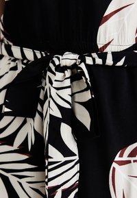Robe noire avec un motif de feuilles blanches et bordeaux, dotée d'une taille froncée et d'une ceinture en tissu nouée, fabriquée en coton léger.