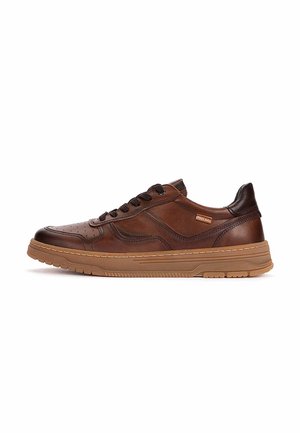 Zapatilla deportiva de cuero marrón con cordones, suela de goma texturizada y pequeña etiqueta de marca en el lateral, mostrada de perfil sobre fondo blanco.