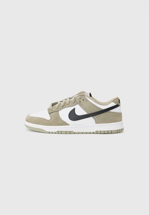 Sneakers scamosciati beige e bianchi con accenti neri, punta perforata, lacci piatti e suola in gomma con un motivo di grip testurizzato.