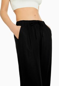 Svarta, löst sittande byxor i lätt tyg, med elastiskt midjeband och snörning samt sidofickor.