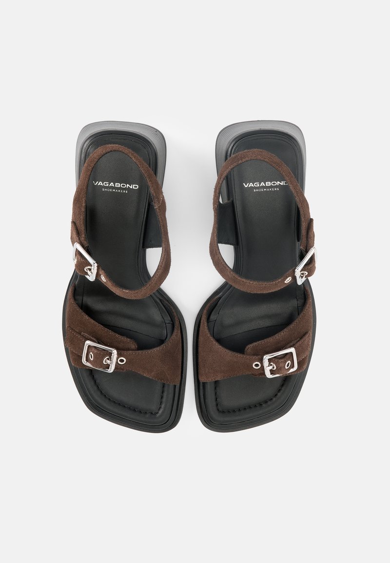 Paar schwarze Sandalen mit braunen Wildlederriemen und silbernen Schnallen, quadratische Zehen und "Vagabond Shoemakers"-Markierung auf den Innensohlen.