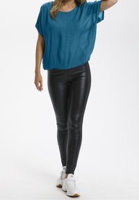 Top corto a maniche corte di colore teal e textura abbinato a leggings neri lucidi e sneaker bianchi. L'outfit presenta una vestibilità comoda e una silhouette aderente.
