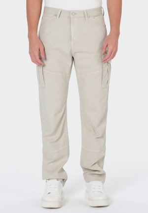 Beige cargo pants with side pockets worn with white sneakers and a white top, shown from waist to feet against a plain background.