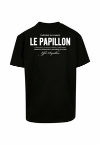 Sort t-shirt i sort bomuld med hvid tekst på ryggen, inklusive "THÉORIE DU CHAOS LE PAPILLON" og et citat om, at små ændringer kan påvirke resultater.