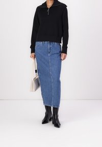 Black zip-up sweatshirt, blue denim maxi skirt, knee-high black boots with square toes, and a small silver handbag.