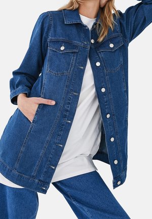 Denim jacket in dark blue, featuring a button-up front, two chest pockets, and long sleeves. Finished with white stitching and silver buttons.