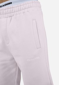 Pantalones de chándal de color rosa claro con una textura suave, que cuentan con una cinturilla elástica, bolsillos laterales y un logo "PEGADOR" embellecido en la pierna.