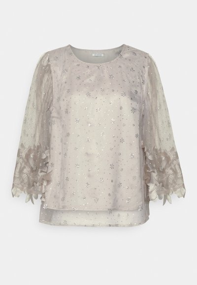 Light beige blouse with sheer, embellished sleeves featuring floral patterns and silver accents. Smooth texture, round neckline, and loose fit.