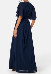 Granatowa sukienka maxi z lekkiego, zwiewnego materiału z falbaniastymi rękawami, dopasowan�ą talią i wiązaniem z tyłu. Okrągły dekolt z guzikiem.