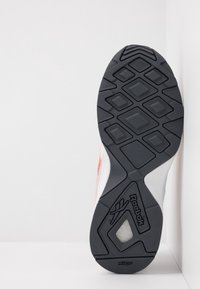 Svart gummi yttersula med diamanttredönster, med en vit mellansula och orange detaljer. Ingen synlig branding på den övre delen.