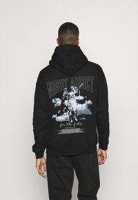Sort hætte sweatshirt med et grafisk print på ryggen af en engel statue, skyer og tekst. Lavet af bomuld. Regular fit.