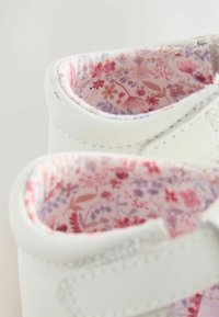 Bottes en cuir blanc avec un col rembourré, dotées d'une doublure en tissu à motif floral rose et d'une fermeture à bande Velcro. Texture lisse et forme ronde.