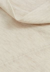 Ljust beige tyg med en mjuk, texturerad yta. Materialet verkar vara stickat med subtila variationer och en slät fall. Synlig sömdetalj.