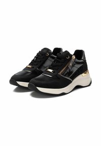 Zapatillas deportivas negras que combinan materiales lisos y texturizados, acentos dorados y una cremallera lateral. Suela blanca gruesa.