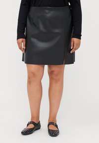 Minifalda de cuero negro con una ligera abertura lateral. Presenta una textura suave y un diseño minimalista, combinada con bailarinas negras adornadas.