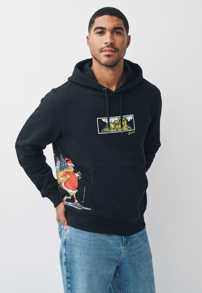 Zwarte hoodie met een Grinch-afbeelding op de borst en kleurrijke feestelijke ontwerpen op de zak. Gemaakt van zachte stof met een buidelzak.